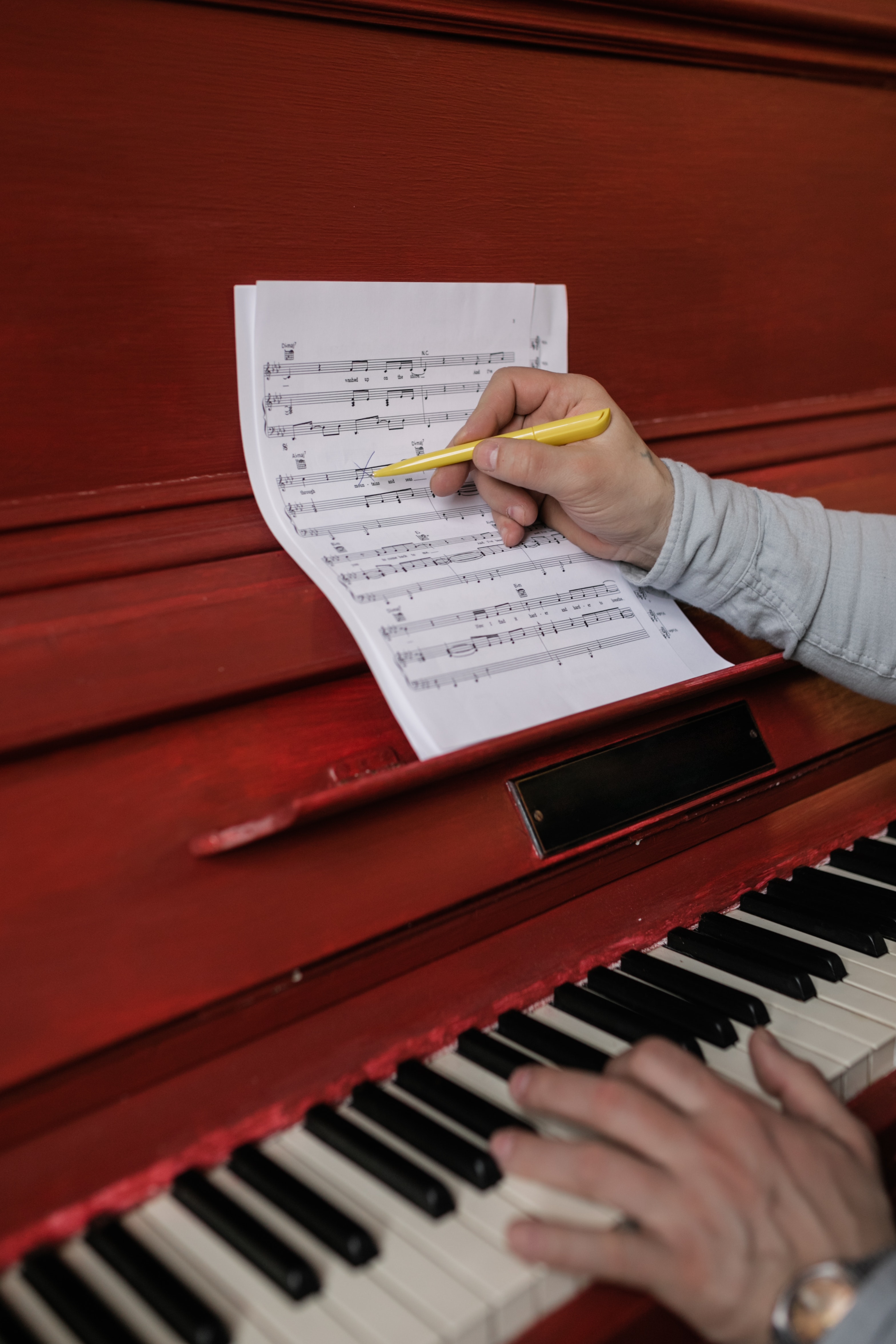 Person playing the piano and taking notes on music sheet